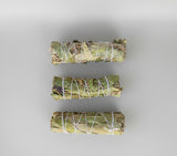 Three bundles of sage tied with twine on a light gray background