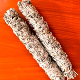 Two bundles of sage smudge sticks on a red background