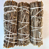 Three bundles of sage sticks tied with white string on a light background