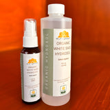 Two bottles of Sun Grown Organic White Sage Hydrosol on a red background