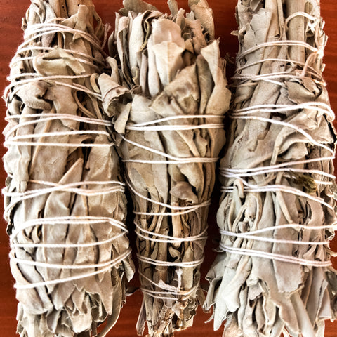 Three bundles of sage wrapped in twine on a wooden surface