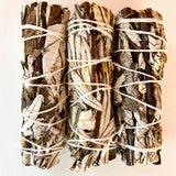Three bundles of yerba san tied together on a light pink backgrounda