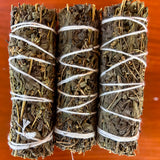 Three bundles of black sage tied together with white string on a red background