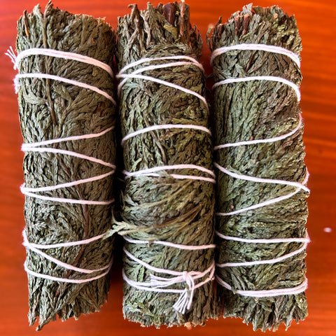 Three smudge sticks of cedar tied with white string on a red background
