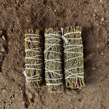Three bundles of juniper tied with twine on a dirt surface