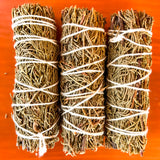 Three bundles of juniper wrapped with white string on an orange background