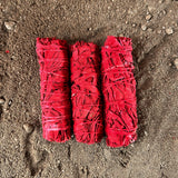 Three red bundles of sage sticks on a sandy surface