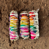 Three colorful smudge sticks on a sandy surface