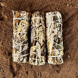 Three yerba sante smudge sticks tied with white string on a brown sandy background