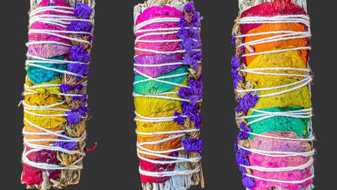 Three colorful smudge sticks with floral elements on a grey surface