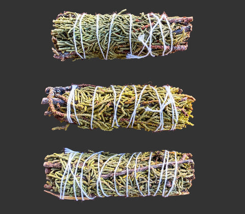 Three bundles of juniper tied with twine on a grey surface