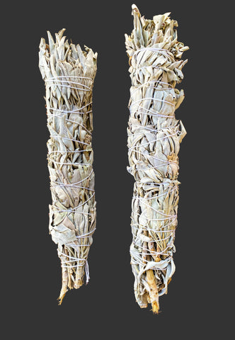 Two sage smudge sticks tied with twine on a wooden surface