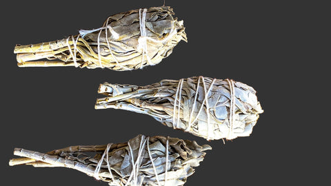 Five bundles of sage wrapped in twine on a grey back ground 
