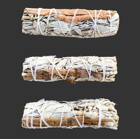 Three bundles of sage with cinnamon wrapped in twine on a wooden surface